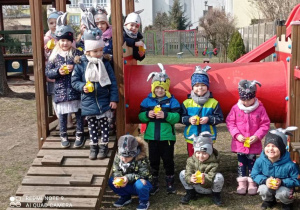 Zdjęcie grupowe w ogrodzie przedszkolnym - dzieci prezentują odnalezione kurczaczki.
